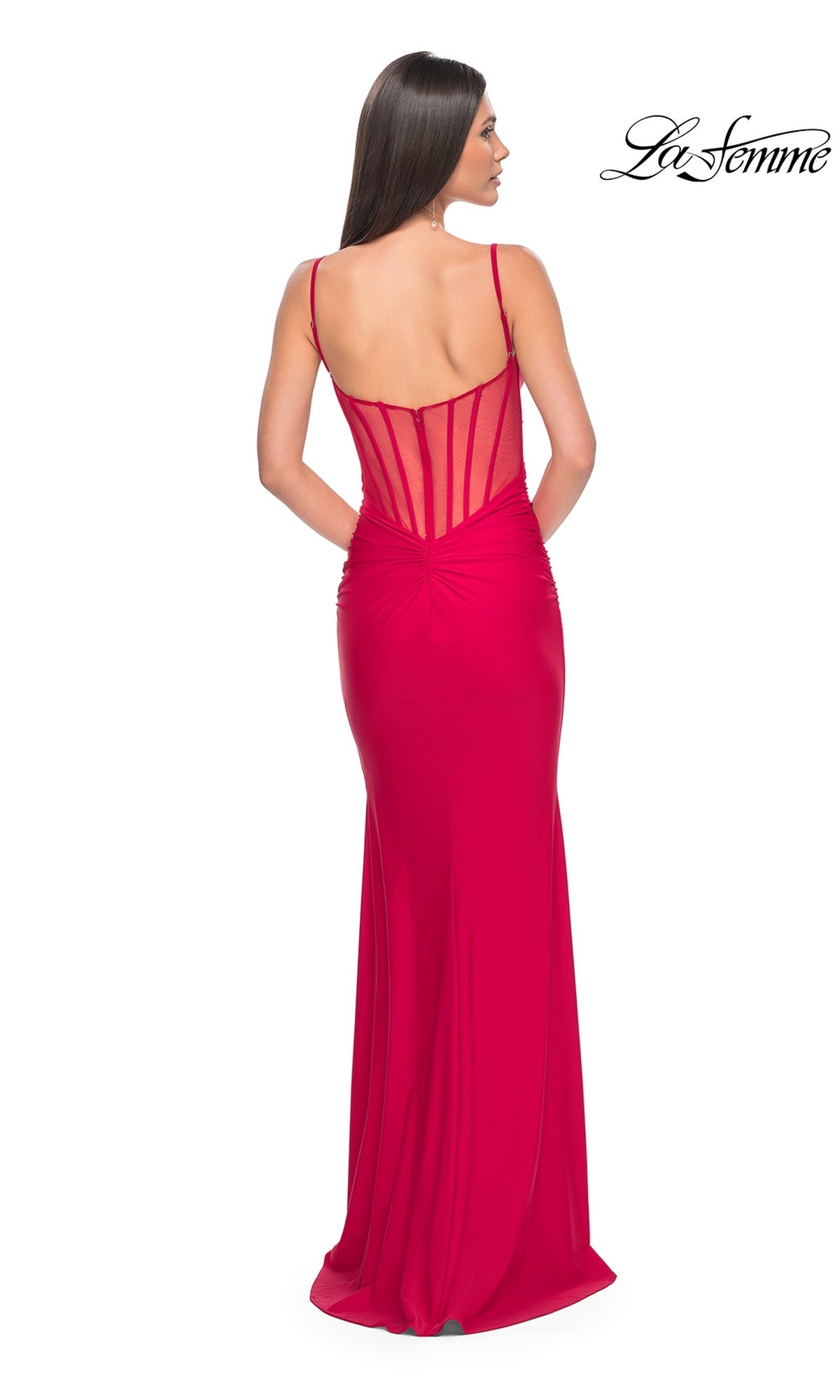 A woman wears the La Femme Sheer-Back Long Jersey Prom Dress 32153, a floor-length red gown with spaghetti straps and a sheer corset-style back, standing against a white background.